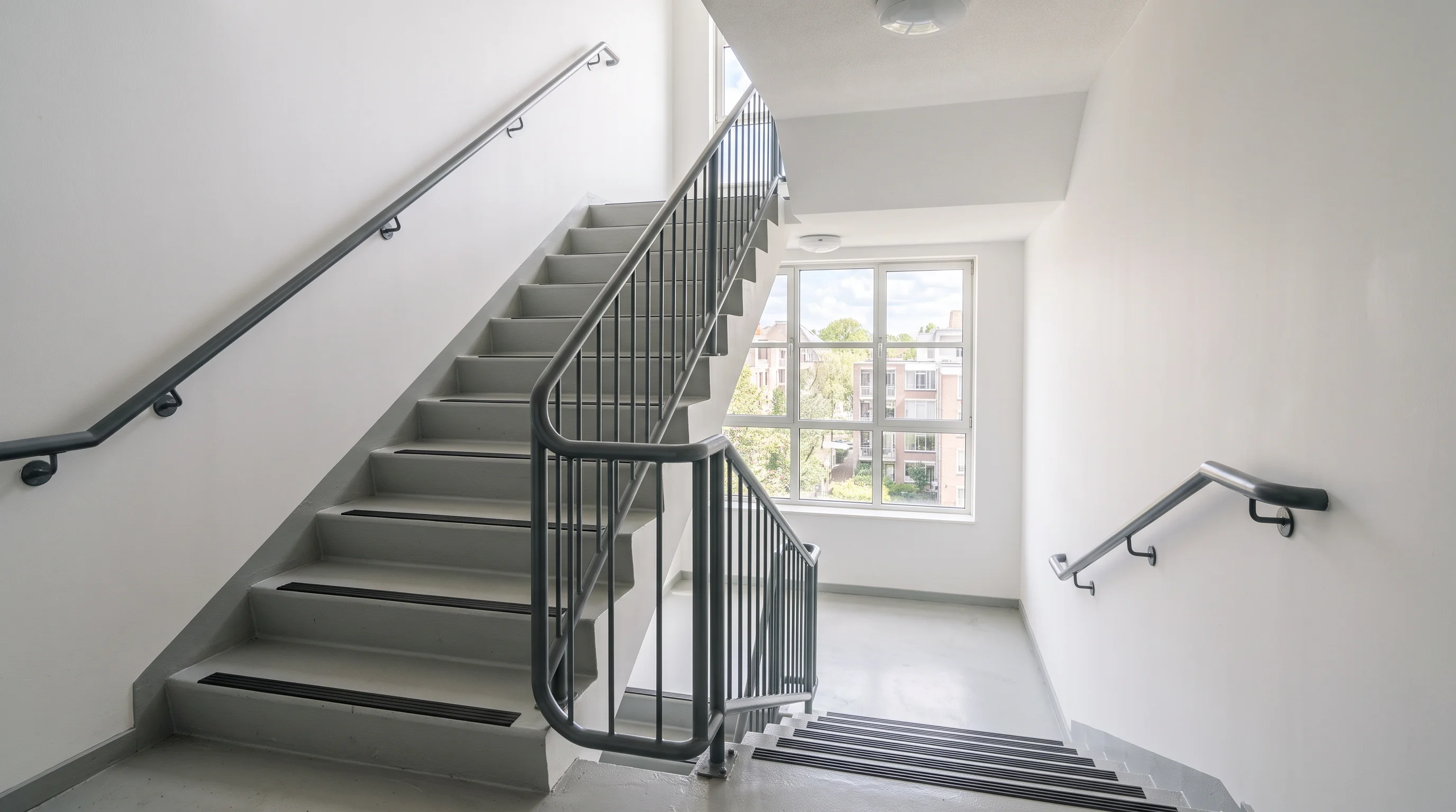 A clean, freshly painted apartment-building stairwell with a simple metal handrail turning at a daylight landing — the register of a well-kept walk-up